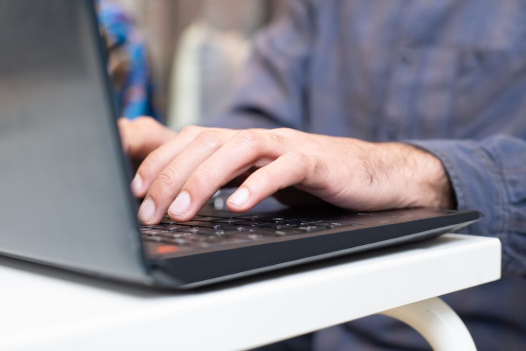 Zwei Hände tippen auf einem Laptop.